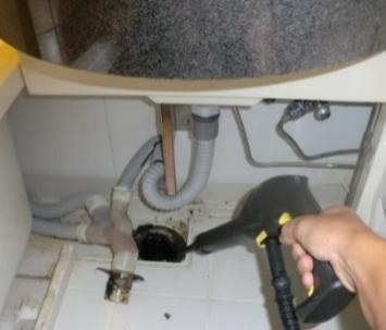 洗面台下の排水トラップを、小型の機材で洗浄している様子